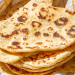 Stack of freshly cooked yogurt flatbreads with yogurt dip on a wooden table.