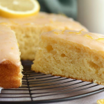 Sliced lemon yogurt cake on a floral plate with fresh lemon slices and glaze, showcasing its moist texture.