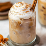 A refreshing glass of pumpkin spice cold brew with autumn leaves and a cinnamon stick on a rustic wooden table.