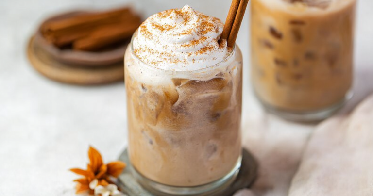 A refreshing glass of pumpkin spice cold brew with autumn leaves and a cinnamon stick on a rustic wooden table.