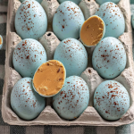 Decorated peanut butter Easter eggs with cocoa speckles on a pastel plate, surrounded by spring flowers.