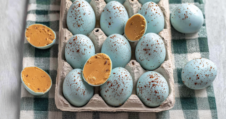 Decorated peanut butter Easter eggs with cocoa speckles on a pastel plate, surrounded by spring flowers.