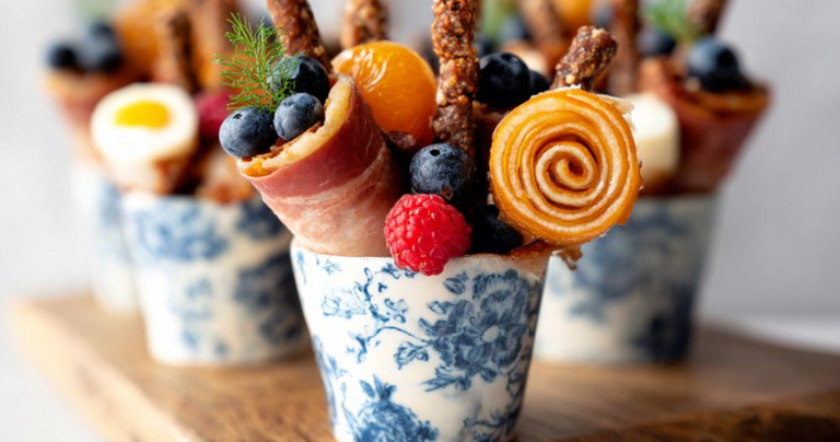 Close-up of vibrant Breakfast Charcuterie Cups filled with fresh fruits, prosciutto, and cheese on a wooden table.