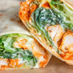 Buffalo chicken caesar salad wrap cut in half, revealing fresh lettuce, diced chicken, and a creamy dressing.