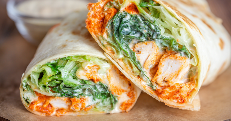 Buffalo chicken caesar salad wrap cut in half, revealing fresh lettuce, diced chicken, and a creamy dressing.