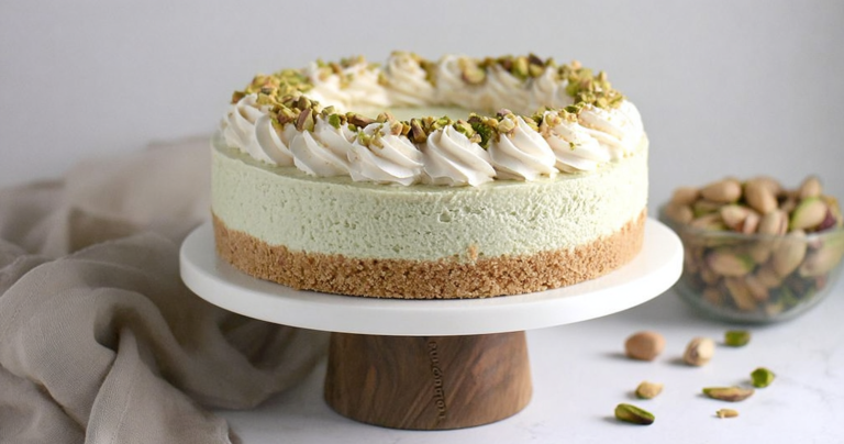Slice of no bake pistachio cheesecake with whipped cream and chopped pistachios on a plate.