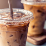 Refreshing glass of iced coffee with ice cubes, whipped cream, coffee beans, and mint garnish.