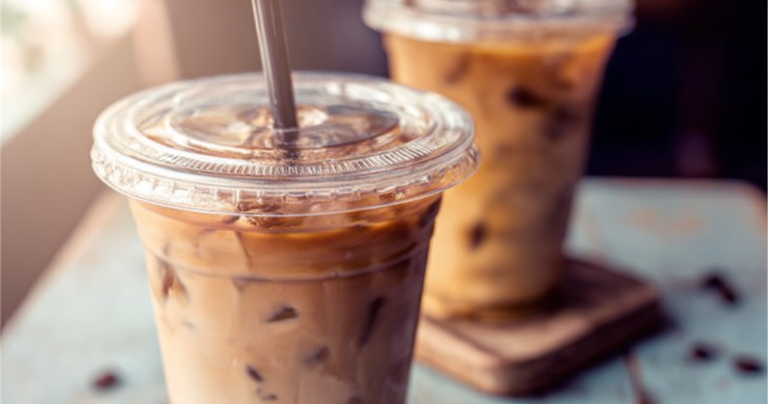 Refreshing glass of iced coffee with ice cubes, whipped cream, coffee beans, and mint garnish.