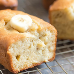 Freshly baked cream cheese banana bread on a wooden table with a slice revealing its moist interior.