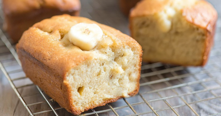Freshly baked cream cheese banana bread on a wooden table with a slice revealing its moist interior.