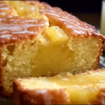 Freshly baked pineapple bread sliced to show the moist texture, garnished with pineapple pieces and glaze, on a wooden cutting board with tropical decor.