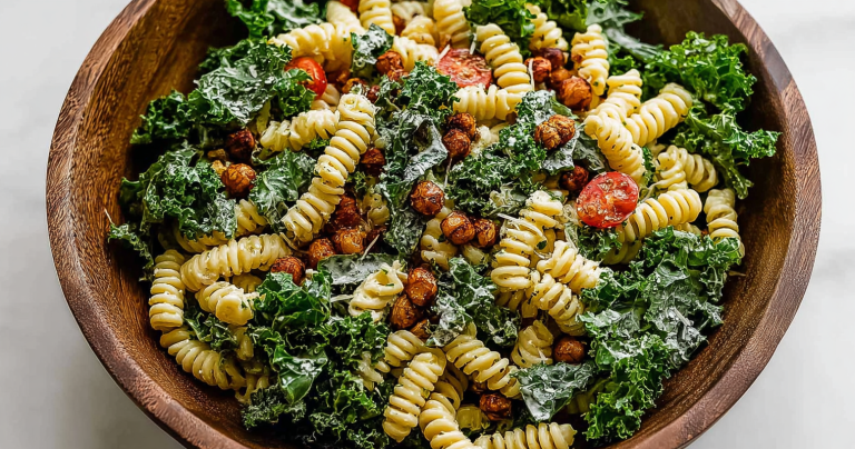 Delicious Kale Caesar Pasta Salad with roasted chickpeas, kale, and lemon on a wooden table.