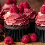 Close-up of chocolate raspberry cupcakes with raspberry frosting and fresh raspberry decorations.