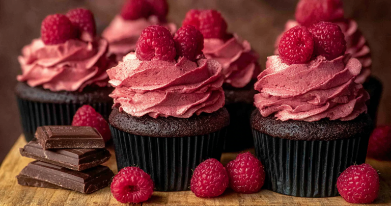 Close-up of chocolate raspberry cupcakes with raspberry frosting and fresh raspberry decorations.