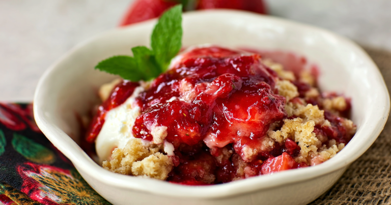 Delicious strawberry cobbler in a bowl with vanilla ice cream on top served on a wooden table.
