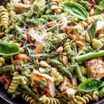 Delicious grilled chicken and asparagus pesto pasta garnished with fresh basil and pine nuts in a bowl.