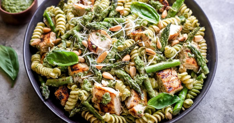 Delicious grilled chicken and asparagus pesto pasta garnished with fresh basil and pine nuts in a bowl.