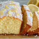 Sliced coconut lemon loaf cake served on a white plate with fresh lemon slices and shredded coconut, displayed on a rustic wooden table.