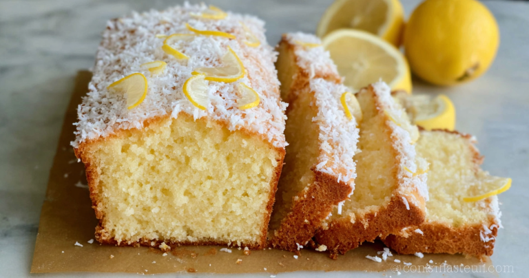 Sliced coconut lemon loaf cake served on a white plate with fresh lemon slices and shredded coconut, displayed on a rustic wooden table.