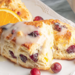 Freshly baked cranberry orange scones with orange glaze on a wooden table, garnished with orange slices and cranberries.