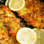 Crispy air fryer parmesan crusted cod on a wooden table with lemon wedges and fresh herbs.