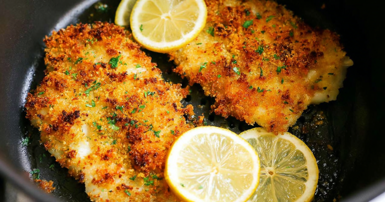 Crispy air fryer parmesan crusted cod on a wooden table with lemon wedges and fresh herbs.