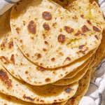 Freshly cooked yogurt flatbread with dips and herbs on a wooden board.