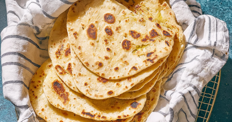 Freshly cooked yogurt flatbread with dips and herbs on a wooden board.