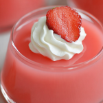 Bowl of Greek yogurt jello with whipped cream and strawberries on a wooden table