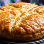 Sliced galette des rois with almond filling on a wooden table, decorated for Epiphany celebrations.