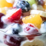 Delicious creamy yogurt fresh fruit salad with vibrant strawberries, peaches, bananas, and red seedless grapes in a bowl.