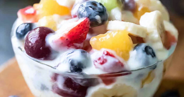 Delicious creamy yogurt fresh fruit salad with vibrant strawberries, peaches, bananas, and red seedless grapes in a bowl.