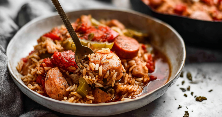 A colorful bowl of jambalaya with chicken, sausage, and vegetables on a wooden table.