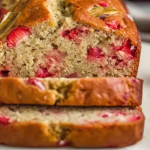 A delicious slice of strawberry banana bread garnished with fresh strawberries and banana slices on a white plate.