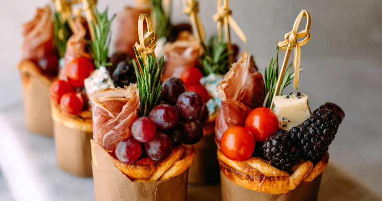 Colorful individual charcuterie cups filled with meats, cheeses, and fruits on a wooden board.