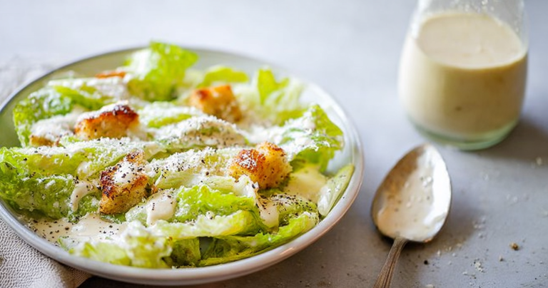 Creamy homemade Caesar salad dressing in a bowl, garnished with fresh herbs and Parmesan cheese.