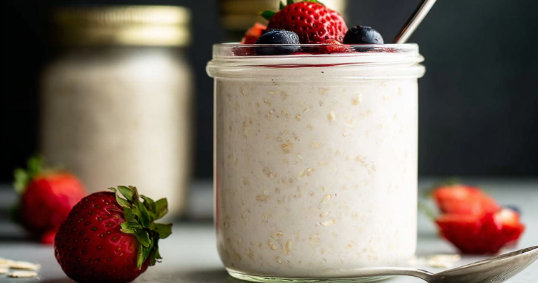 Bowl of yogurt overnight oats topped with mixed berries and banana on a wooden table.