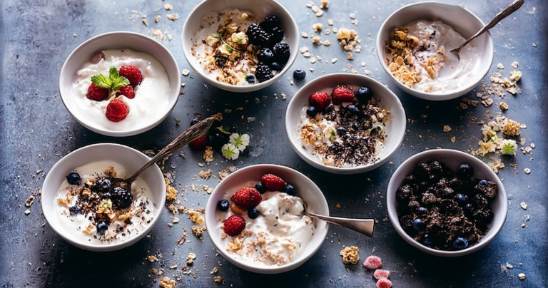 A vibrant yogurt bowl adorned with sliced strawberries, blueberries, almonds, and a drizzle of honey on a wooden table.