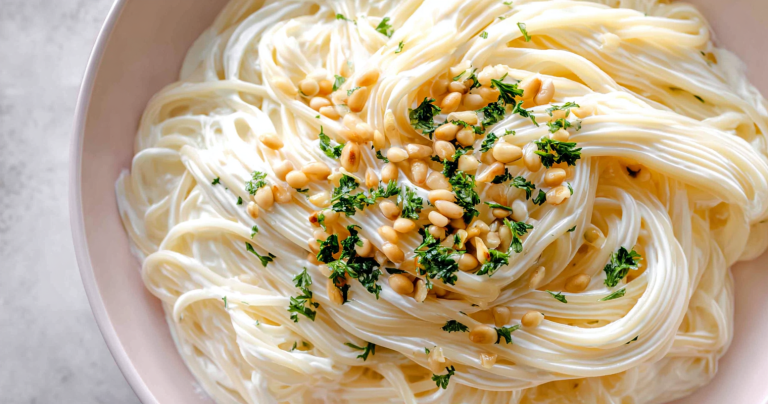 Creamy yogurt pasta sauce with spaghetti garnished with pine nuts and herbs.