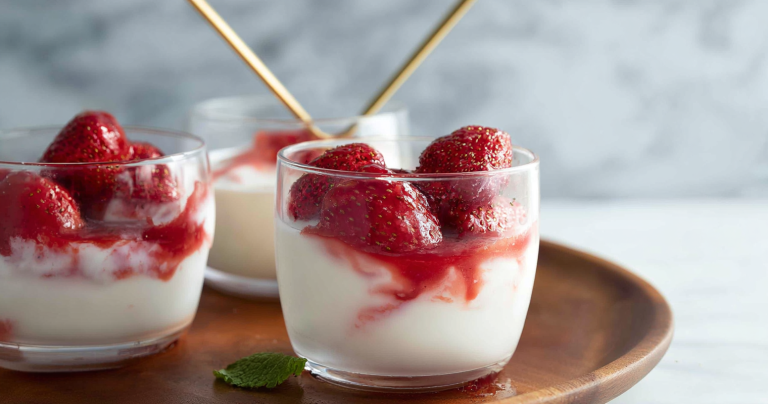 Close-up of roasted strawberries drizzled with honey, served in a white bowl with fresh mint garnish.