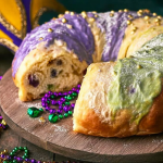 Decorated cream cheese stuffed king cake with purple, green, and gold sugar on a festive table for Mardi Gras.