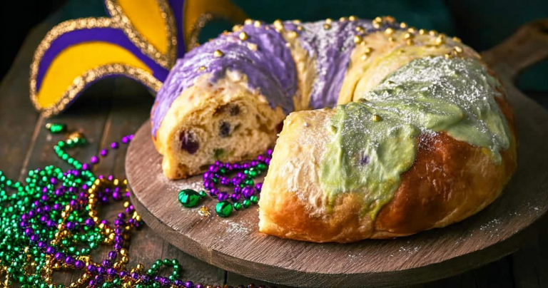 Decorated cream cheese stuffed king cake with purple, green, and gold sugar on a festive table for Mardi Gras.