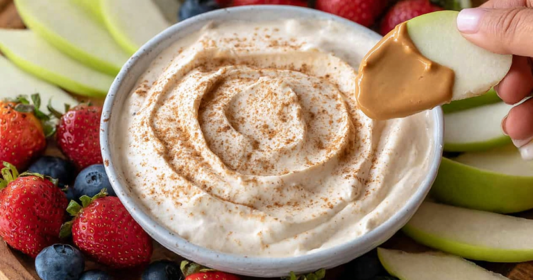 Peanut butter yogurt dip with fresh apple slices and strawberries on a wooden table.