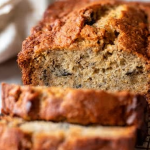 Sliced banana bread on a wooden cutting board with fresh bananas and walnuts.