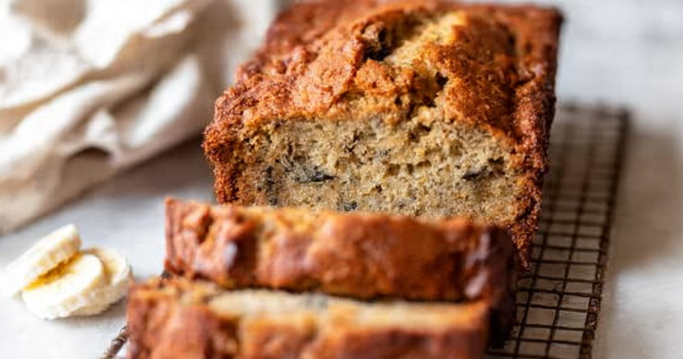 Sliced banana bread on a wooden cutting board with fresh bananas and walnuts.