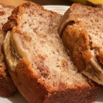 Sliced banana bread on a cutting board with ripe bananas in the background