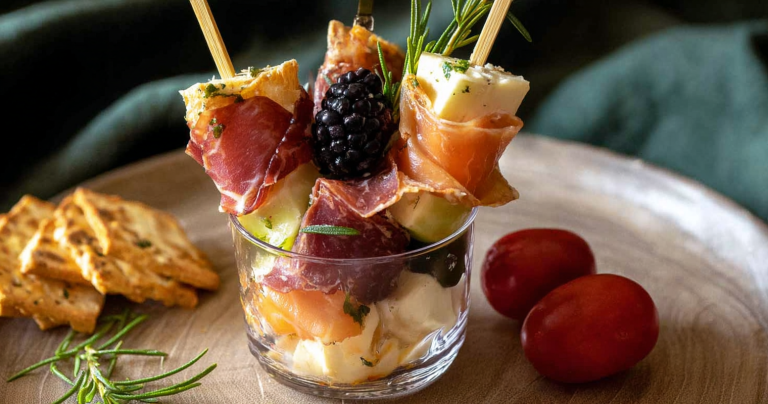 Colorful individual charcuterie cups filled with cheese, meats, fruits, and nuts on a festive table setting.