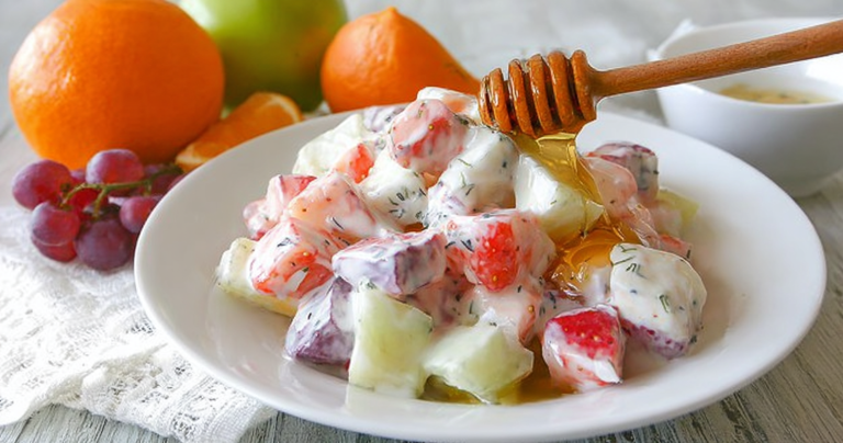 Colorful creamy yogurt fruit salad with fresh strawberries, blueberries, and sliced bananas, topped with honey.