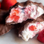 Frozen chocolate strawberry yogurt clusters on a plate with fresh strawberries.