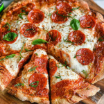 Homemade Greek yogurt pizza topped with fresh vegetables and cheese on a wooden peel.